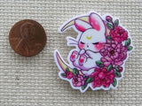 Second view of White bunny is sleeping on a bed of red and pink flowers in a crescent moon minder.